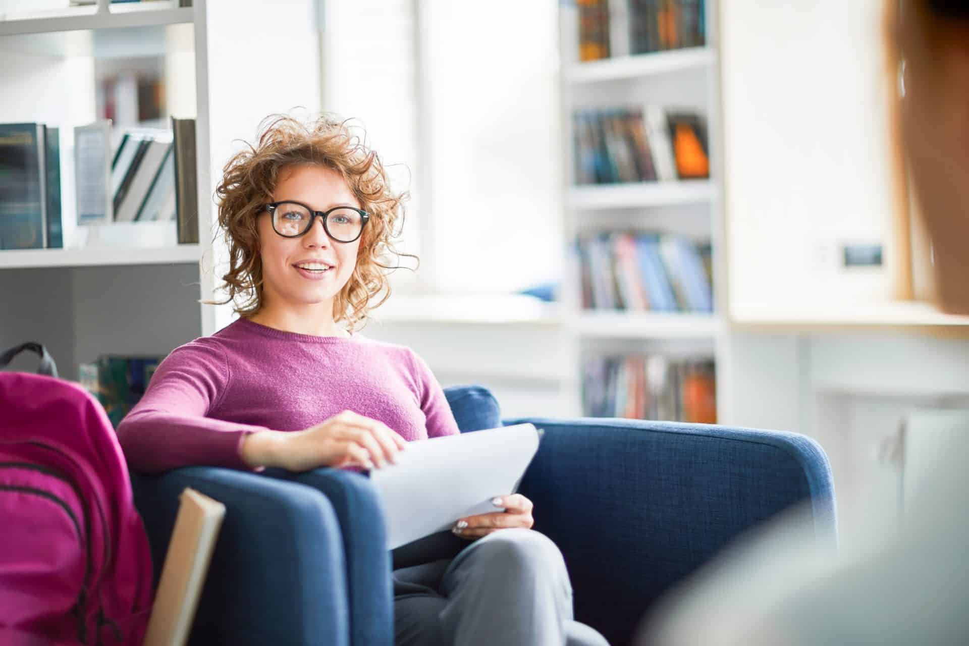 Female college student wearing eyeglasses sitting and discussing her report with her classmates