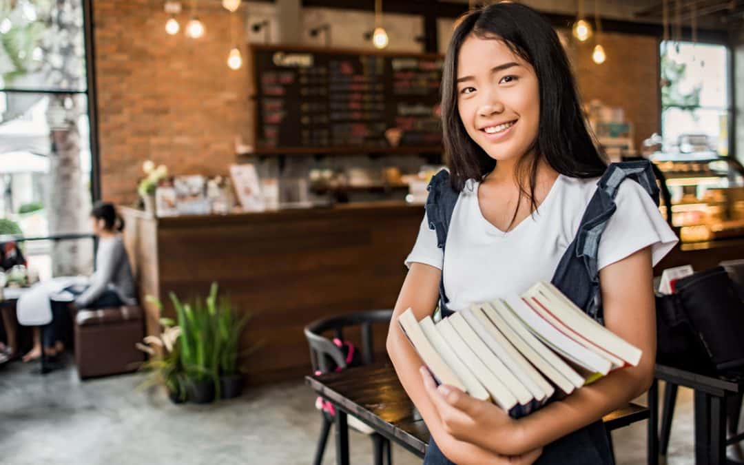 student in coffee shop holding books